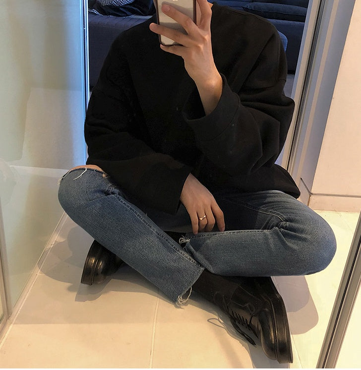 Round Neck Sweater Men's And Women's worn with jeans and black boots, seated pose in a modern interior.