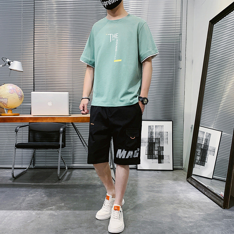 Casual Summer New Men's Hip-hop outfit featuring a green t-shirt and black shorts in a modern workspace.