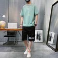 Casual Summer New Men's Hip-hop outfit featuring a green t-shirt and black shorts in a modern workspace.