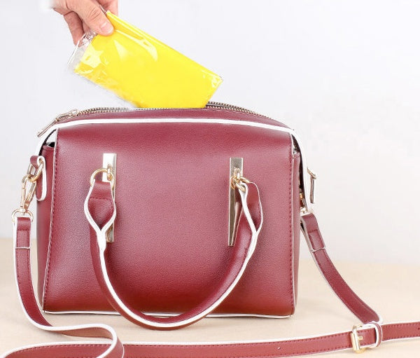 Person placing a yellow item into a stylish red handbag with gold accents.